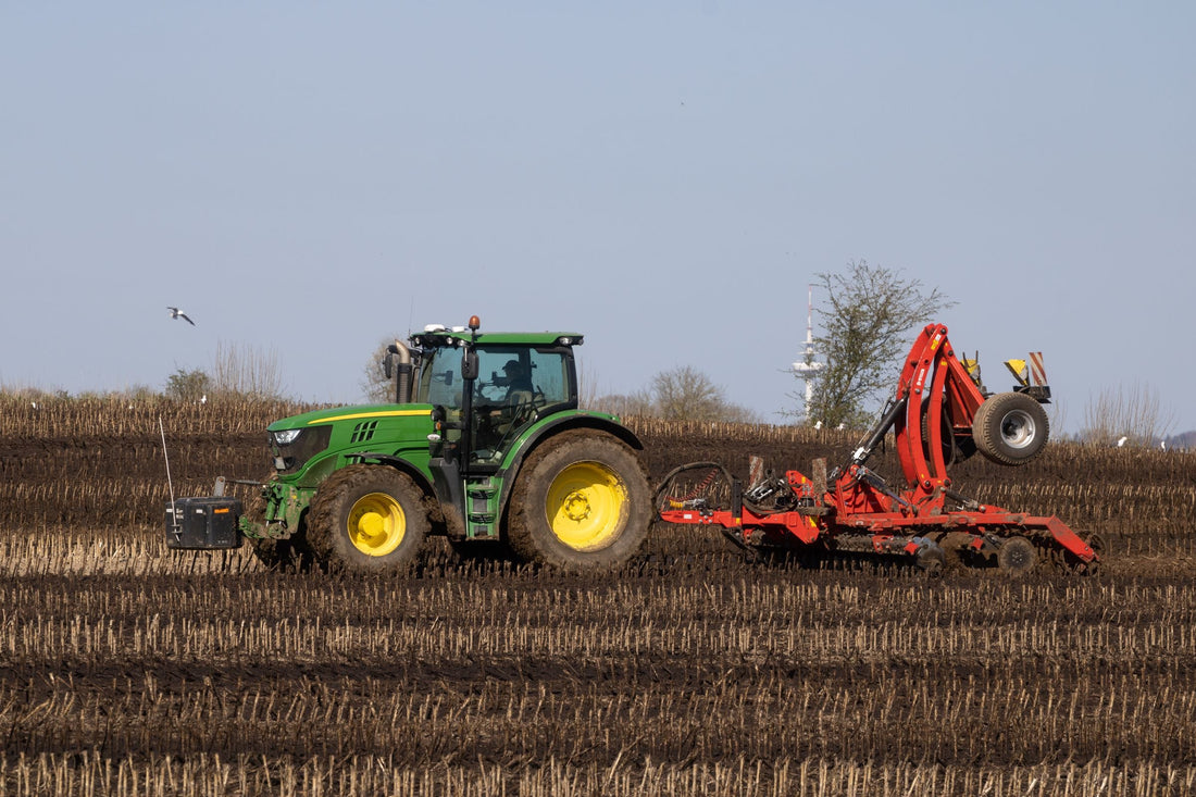 John Deere tractor pulling a red disc harrow through Iowa cropland