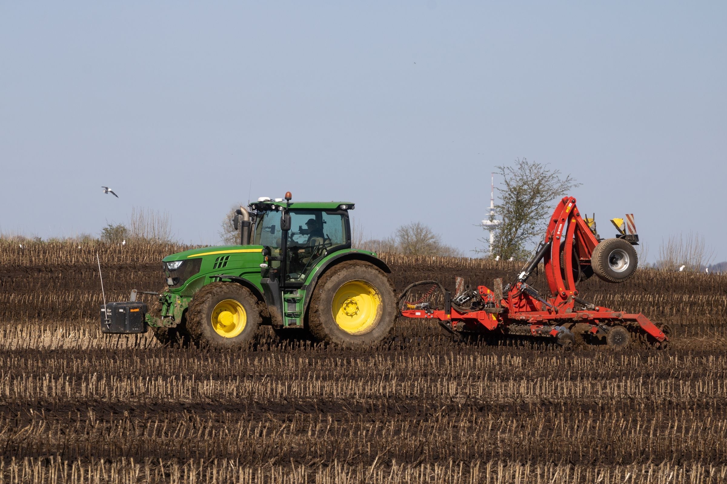 John Deere tractor pulling a red disc harrow through Iowa cropland